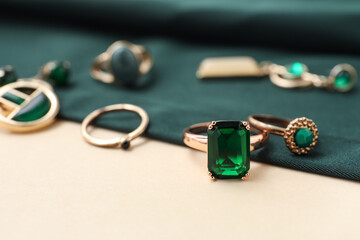 Stylish female jewelry with green stone on piece of cloth on beige background. Closeup