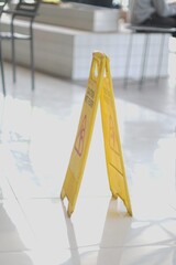 Bright yellow 'Caution Wet Floor' sign on a reflective white tile floor in a public building,...