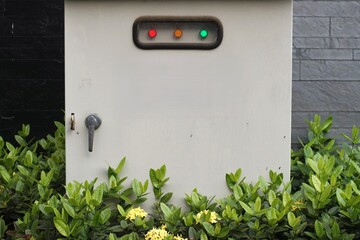 Outdoor electrical control box with indicator lights and handle surrounded by green plants and...