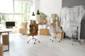 Blurred view of office with desks, plants and boxes on moving day