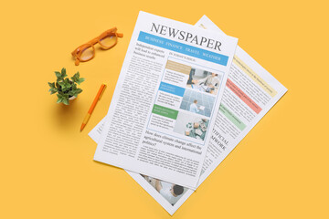 Newspaper, eyeglasses, houseplant and pen on yellow background. Top view