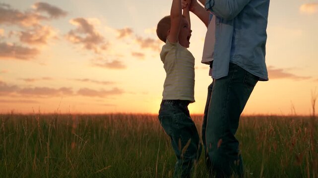 Dad playing with baby son holding his hands on lawn. Dad jumping with little son in nature park. Family in park. Happy family playing in park in summer. Childhood dream concept. Father raising child.
