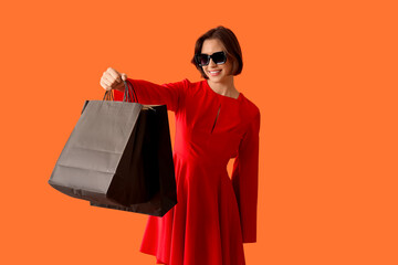 Beautiful young woman with shopping bags on orange background. Black Friday concept