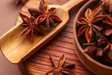 Wooden board with bowl of aromatic star anise and scoop on color background, closeup