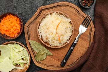 Delicious sauerkraut in bowl with ingredients on black background. Top view