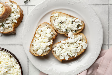 Plate of bread slices with fresh cottage cheese on white tile background