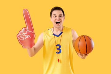 Male sports fan with foam hand and ball on yellow background