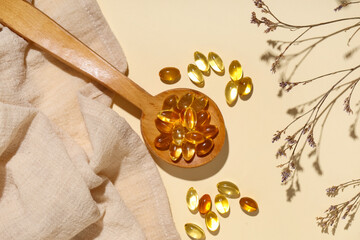 Composition with wooden spoon of fish oil capsules, napkin and dried flowers on color background