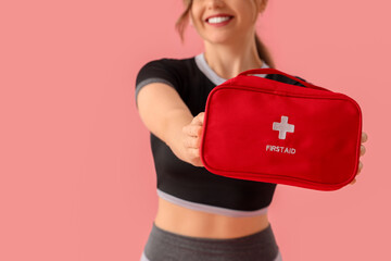 Sporty young woman with first aid kit on pink background, closeup