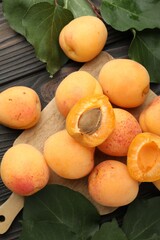 Fresh apricots and green leaves on dark wooden table, flat lay