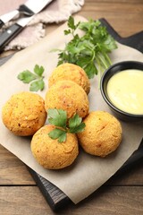 Delicious fried croquette balls with parsley and sauce on wooden table