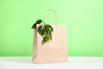 Eco friendly packaging. Paper bag and leaves on white table against light green background