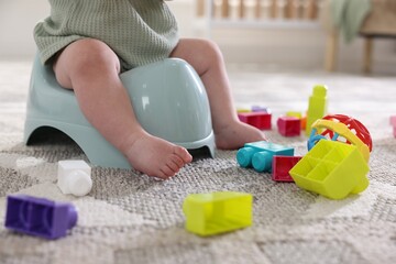 Cute little baby sitting on potty and toys at home, closeup