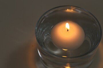 Burning candle in glass of water on table, closeup. Space for text