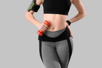 Sporty young woman with dumbbell on light background