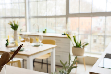 Blurred view of light kitchen decorated for Easter with dining table, plants and counters