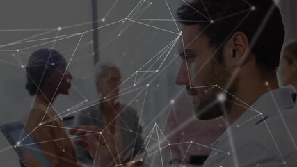 Seated man tapping tablet launching network overlay while team discussing business data analysis - Powered by Adobe