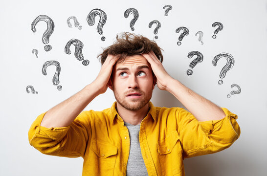 Confused man in yellow shirt stands against white background with question marks around him - Powered by Adobe