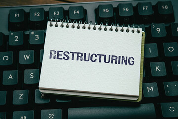 There is notebook with the word Restructuring. It is as an eye-catching image.