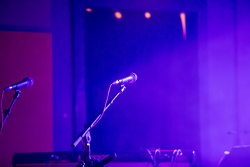 A microphone on a stand on a lit stage before a musical show.