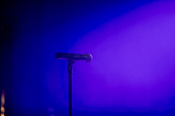 A microphone on a stand on a lit stage before a musical show.