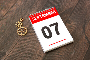 Calendar with date 7 September and flowers on wooden table near color wall.