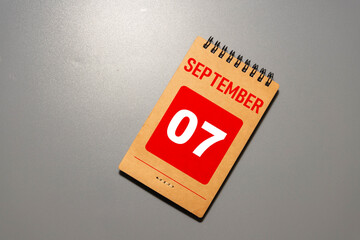 Calendar with date 7 September and flowers on wooden table near color wall.