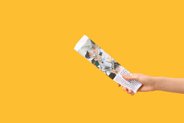 Female hand with newspaper on yellow background
