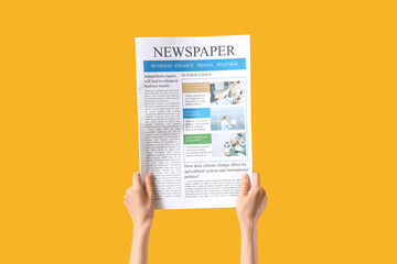 Female hand with newspaper on yellow background