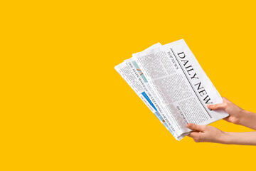Female hands with newspapers on yellow background