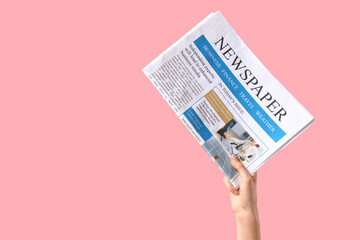 Female hand with newspaper on pink background