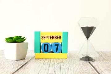 Calendar with date 7 September and flowers on wooden table near color wall.