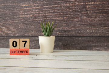 Calendar with date 7 September and flowers on wooden table near color wall.