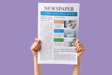 Female hands with newspaper on lilac background