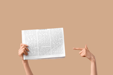 Female hands pointing at newspaper on beige background