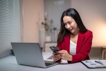 Asian businesswoman using smartphone and working on laptop in office at night
