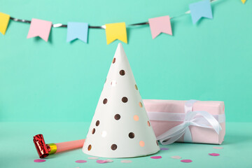 Party hat, whistle, gift box and decor on color background