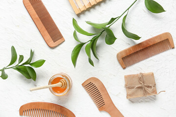 Composition with wooden hair combs, soap bar, honey and plant branches on light background
