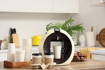 Modern coffee machine with paper cups and capsules on table in kitchen
