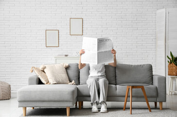 Young woman reading newspaper on sofa at home