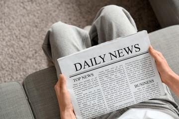 Young woman reading newspaper on sofa at home, top view