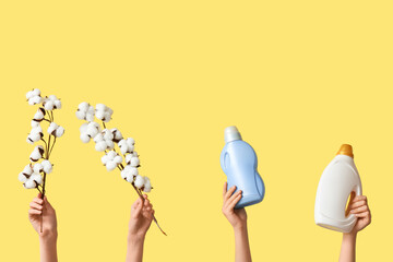 Female hands with cotton flowers and laundry detergents on yellow background