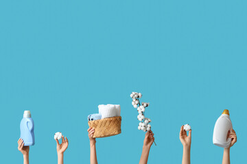 Female hands with cotton flowers, towels and laundry detergents on blue background
