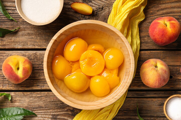 Composition with bowl of canned peaches, fresh fruits and sugar on wooden background