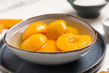 Bowl of tasty canned peaches on light table, closeup