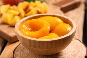 Bowl of tasty canned peaches on wooden table
