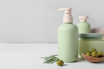 Set of natural cosmetic products and spoon with green olives on light wooden background