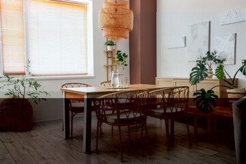 Interior of stylish dining room with wooden table, chairs and houseplant