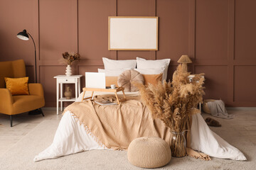 Interior of stylish bedroom with cozy bed, laptop and pampas grass
