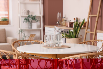 Table with jug and glasses of water in kitchen, closeup